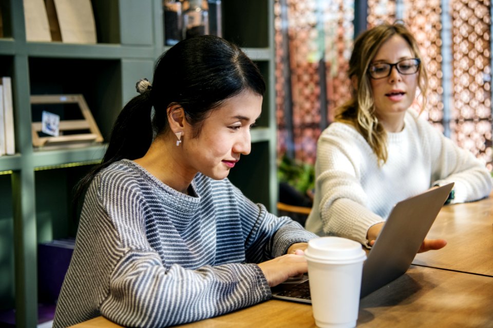 Two Women Sitting In Front Of Brown Wooden Table