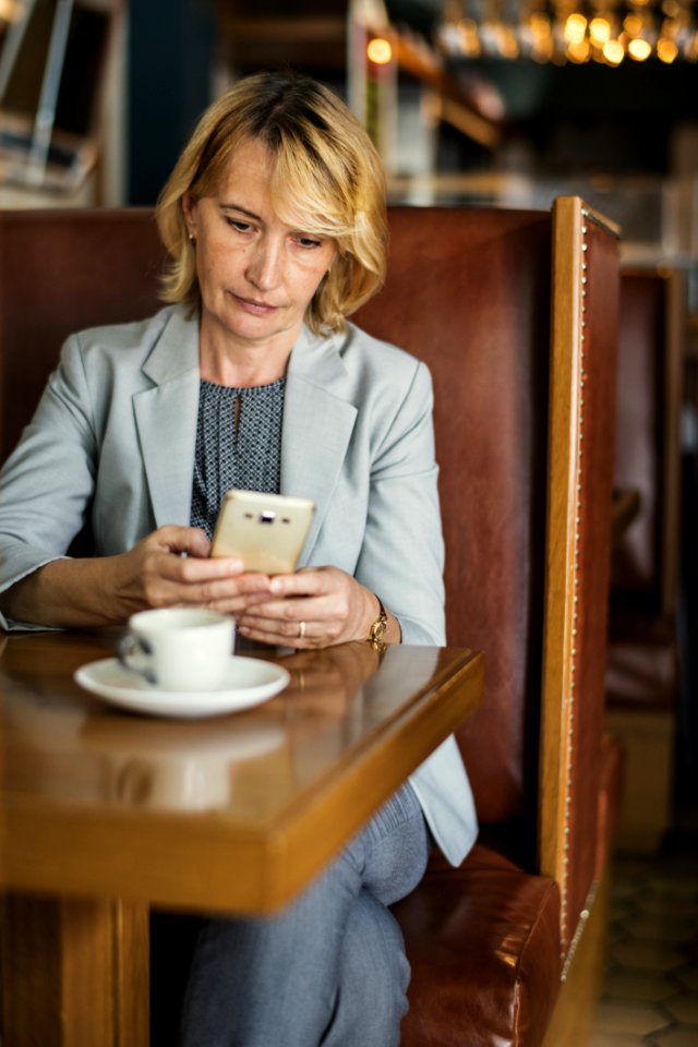 Woman In Grey Notched Lapel Suit Jacket Holding Smartphone Sitting Beside Wooden Table