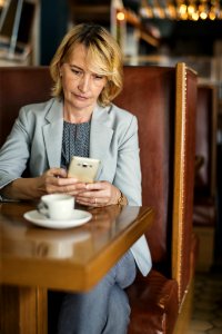 Woman In Grey Notched Lapel Suit Jacket Holding Smartphone Sitting Beside Wooden Table photo