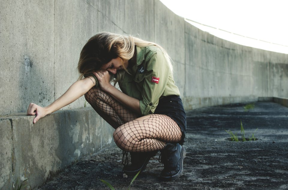 Woman Squatting Near Gray Concrete Wall At Daytime