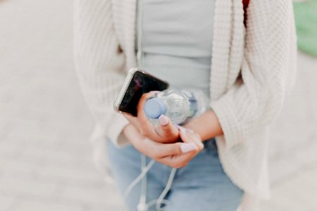 Selective Focus Photography Of Woman In White Cardigan Holding Water Bottle And Black Smartphone photo