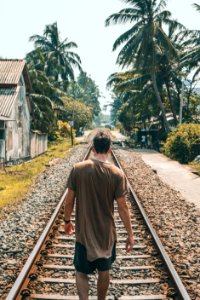 Man In Brown Shirt Standing On Train Rail Near Coconut Palms photo