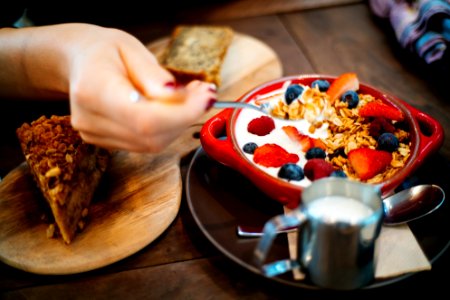 Person Holding Spoon And Round Red Ceramic Bowl With Pastries photo