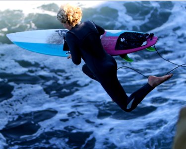 Woman With Surfboard Jumping To Body Of Water photo