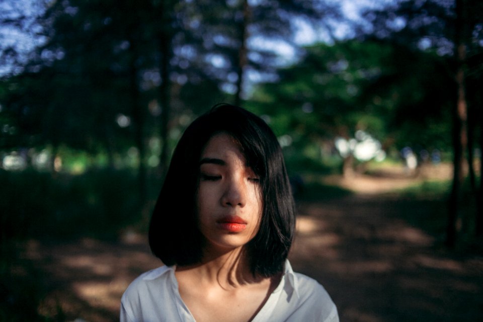 Shallow Focus Photography Of Woman In White Top Beside Green Trees