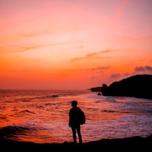 Silhouette Photo Of Man With Backpack Standing In Seashore During Golden Hour photo