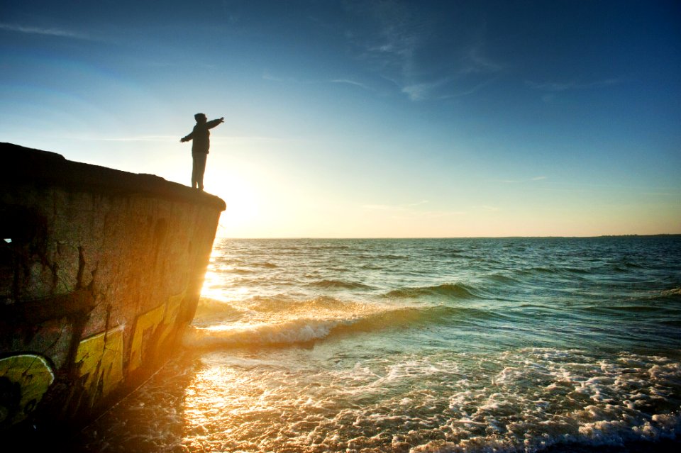 Silhouette Of Person On Cliff Beside Body Of Water During Golden Hour