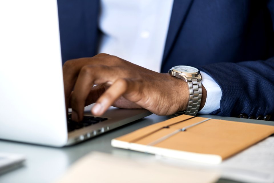 Photo Of Person Wearing Gray Analog Watch Tapping Keyboard Of Laptop