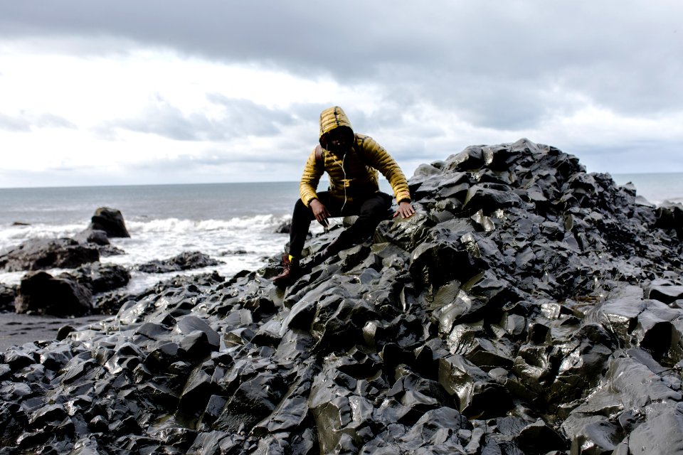 Selective Color Photography Of Man Wearing Hoodie On Stone Behind Body Of Water
