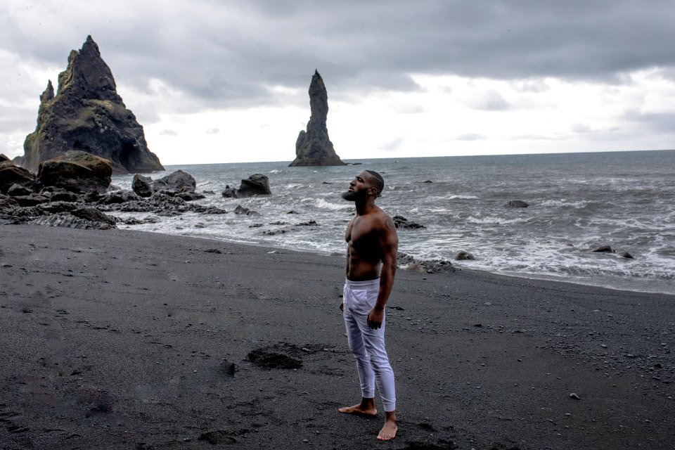 Man In White Jeans Stands On Grey Sand In Beach Under Grey Clouds