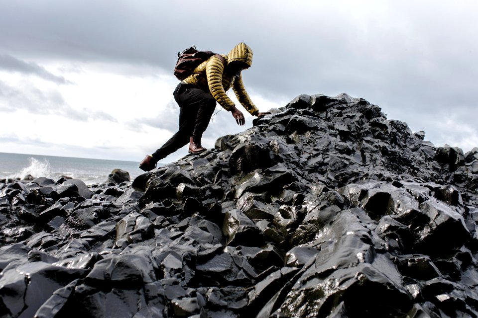 Man Wearing Hoodie And Black Pants Climbing Up Pile Of Rocks photo