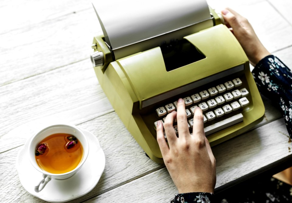 Person Holding Type Writer Beside Teacup And Saucer On Table