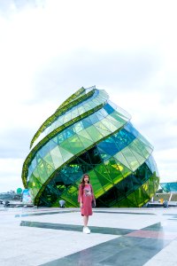 Woman In Pink Long-sleeved Midi Dress Standing Near Green And Blue Landmark Under Gray And White Sunny Cloudy Sky During