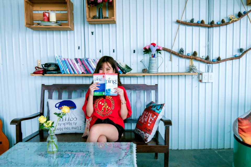 Woman In Red Shirt Holding Book Sitting On Bench In Front Of Coffee Table