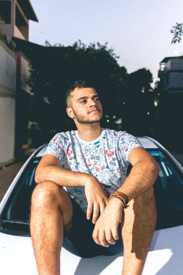 Man In White And Blue Crew-neck T-shirt Sitting On Top Of White Car