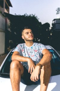 Man In White And Blue Crew-neck T-shirt Sitting On Top Of White Car photo