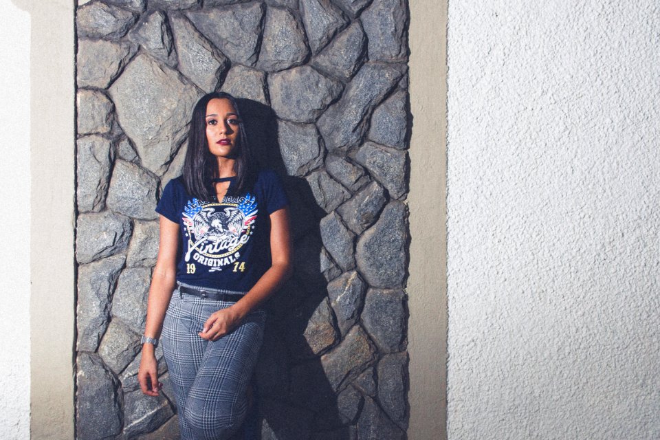 Woman Wearing Blue Wings-printed V-neck T-shirt And Gray Pants Leaning On Gray Rock Cladding photo