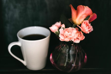 Pink Carnation Flower And Pink Rose Flower In Clear Glass Vase Beside Mug Of Coffee photo