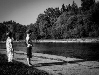 Grayscale Photo Of Oy Boy And Girl Standing Near Body Of Water photo