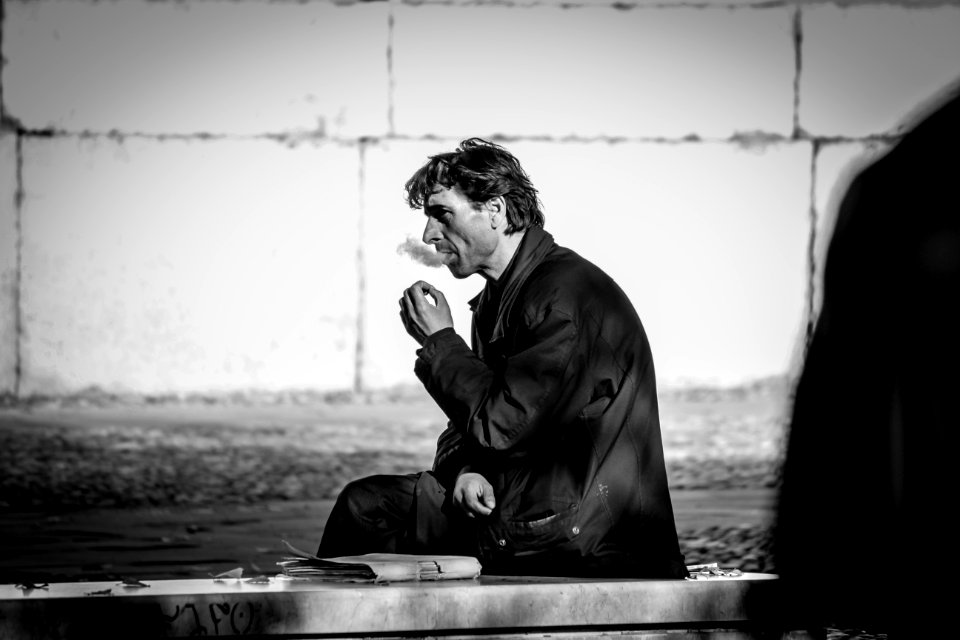 Grayscale Photo Of Smoking Man While Sitting On Bench