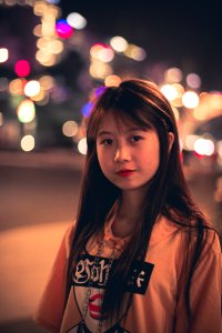 Woman Wearing Pink Black And Red Printed Pullover Hoodie Standing Beside Road Bokeh Photography At Night Time