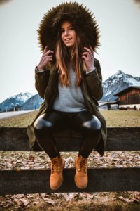 Woman Wearing Brown And Green Parka Sitting On Gray Wooden Fence At Daytime photo