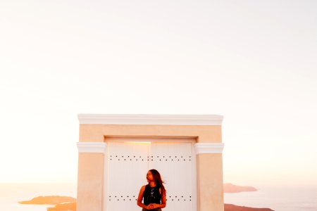 Woman Wearing Black Sleeveless Top Posing In Front Of White Wooden Door