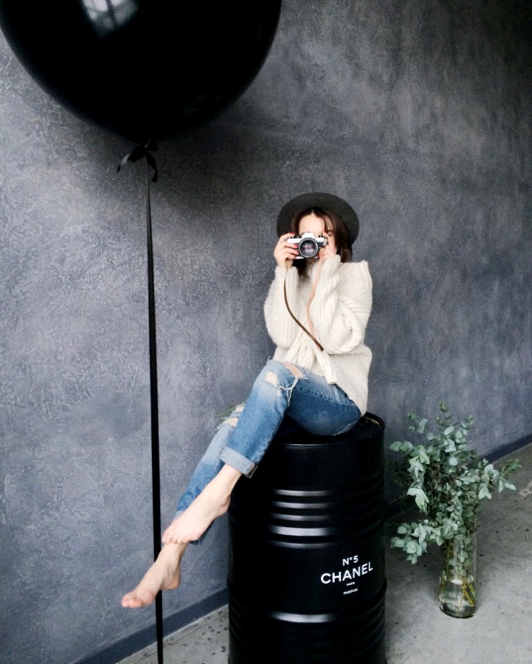 Woman Using Silver Camera Sitting On Black Container Drum