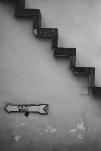 Grayscale Photo Of Exit Signage Under Brown Stairs photo