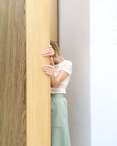 Woman In White Lace Cap-sleeved Top And Green Skirt Hiding Behind Brown Wall