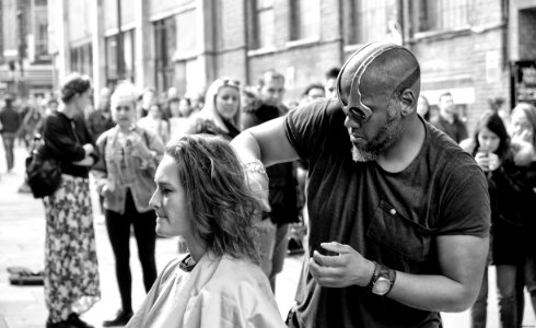Grayscale Photography Of Man Cutting Hair Of Woman Surrounded With People