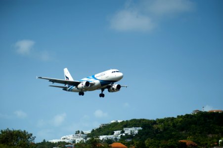 White And Blue Passenger Plane Passing Above Green Tree Covered Hill photo