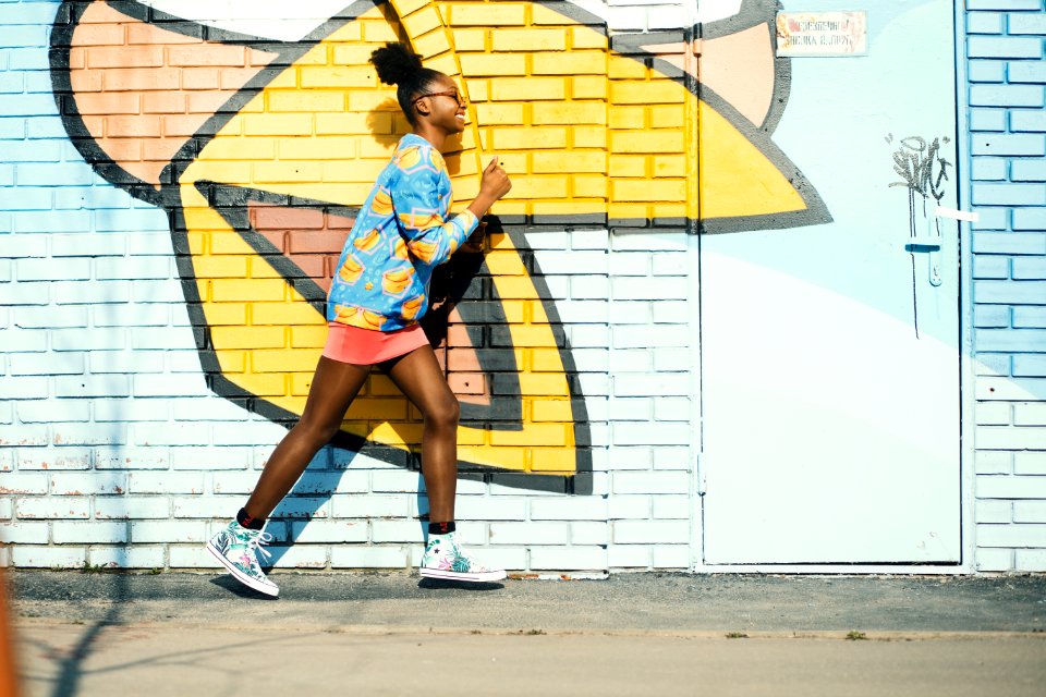 Woman Wearing Blue And Yellow Long-sleeved Shirt Walking Near White And Yellow Painted Wall