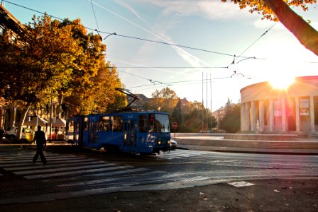 Person Wearing Black Walking On Pedestrian Lane Near Blue Tram Train During Sunset
