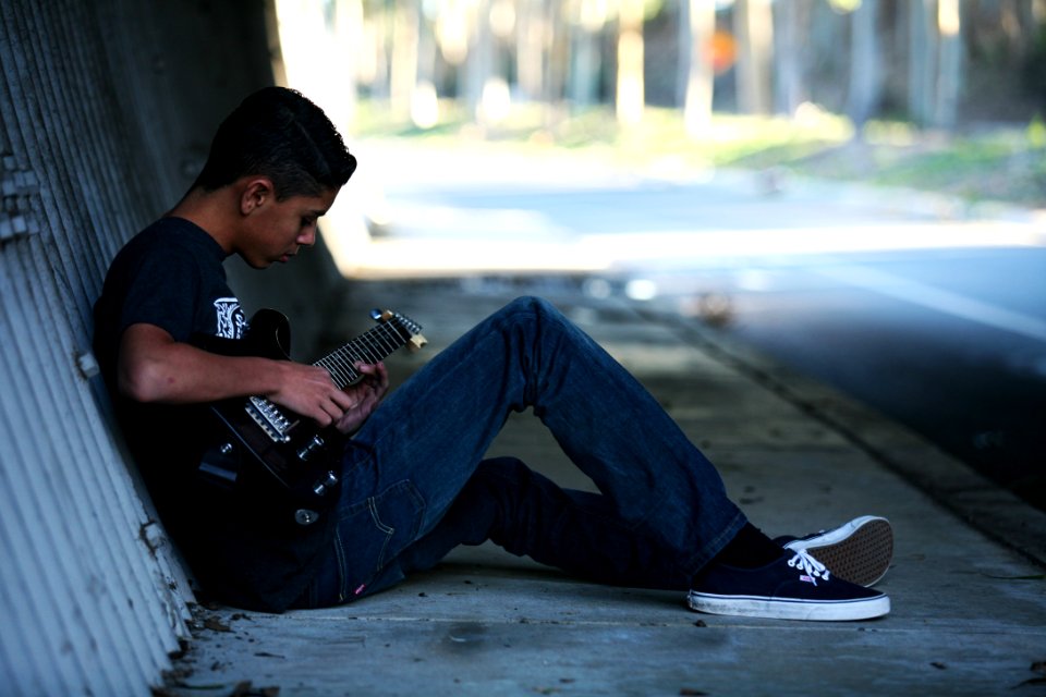 Man Sitting Near Wall Playing Guitar