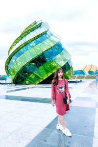 Woman In Red Long-sleeved Top Wearing White Sneakers Walking In Front Of Green And Blue Glass Building photo