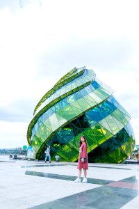 Woman In Red Dress Standing In Front Of Green Glass Elliptical Building photo