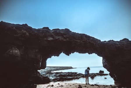 Person Standing On Beach Under Rock