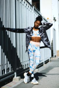 Woman In White Crop Top With Blue Full-zip Jacket And Blue Leggings Posing Near Gray Steel Fence