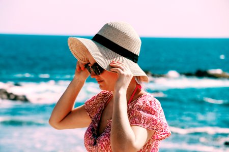 Selective Focus Photo Of Woman Wears Beige Sun Hat Stand Behind Body Of Water A Daytime photo