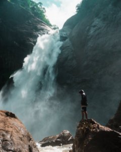 Man Standing On Brown Rock Cliff In Front Of Waterfalls Photography photo