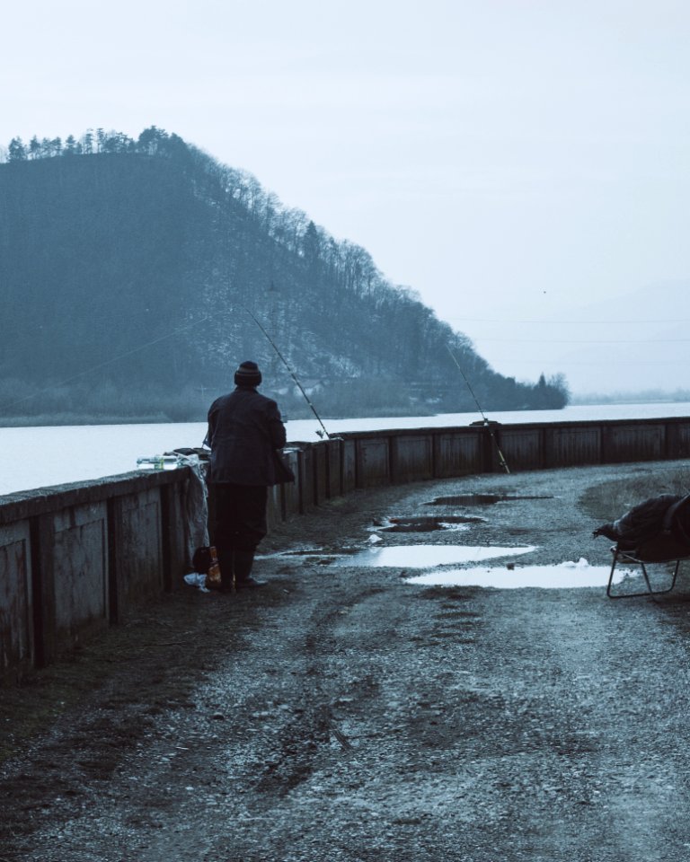 Man Wearing Brown Coat Near A Body Of Water With Fishing Rods At Daytime