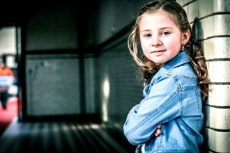 Girl In Blue Denim Jacket Leaning On Gray Wall photo