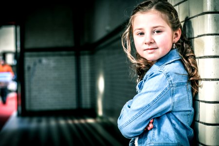 Girl In Blue Denim Jacket Leaning On Gray Wall