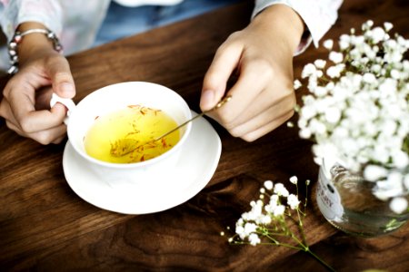 Person Holding Silver Spoon On White Ceramic Teacup With Yellow Liquid Inside photo