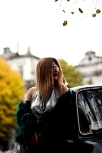 Selective Focus Photography Of Woman Wearing Silver V-neck Sleeveless Top Leaning On Black Car photo