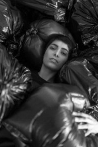 Grayscale Photo Of Female Surrounded By Black Plastic Bags