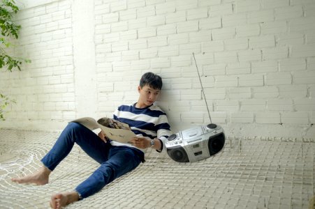 Boy Sitting Near Radio Holding White Catalog