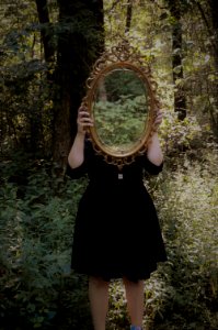 Woman Holding Mirror Against Her Head In The Middle Of Forest photo