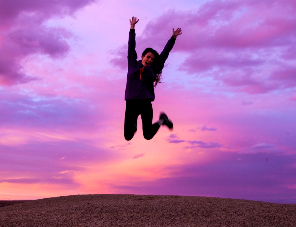 Smiling Woman Wearing Black Jacket And Pants Jumping In Brown Open Field photo